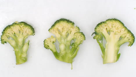 Slow-motion-water-splash-on-three-slices-of-green-broccoli-lying-on-a-white-background-in-the-water